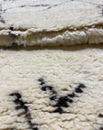 Close-up of a cozy, thick Moroccan rug with a soft cream base and dark intricate patterns displayed on Santa Barbara Chic Moroccan product page.