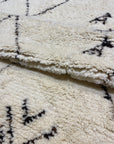 Close-up of a soft, textured Moroccan rug with geometric patterns in black on an off-white background.